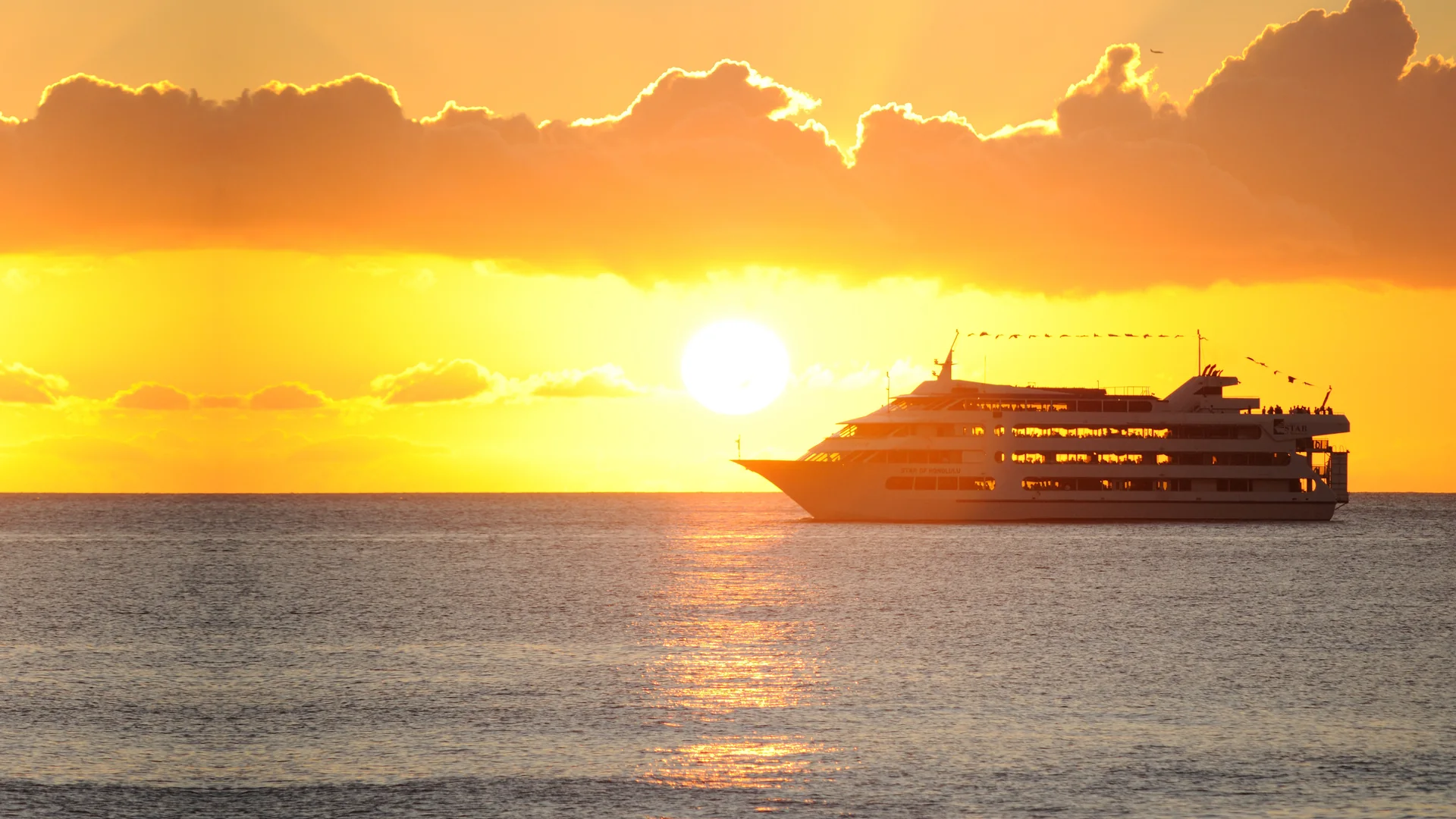 The four-deck Star of Honolulu cruising under glowing clouds across a golden sunset sea off Honolulu